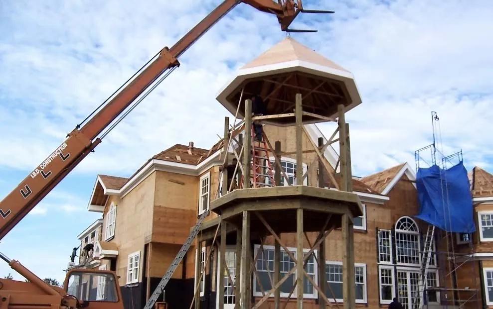 IBD Construction crane lifting a cupola onto a house under construction