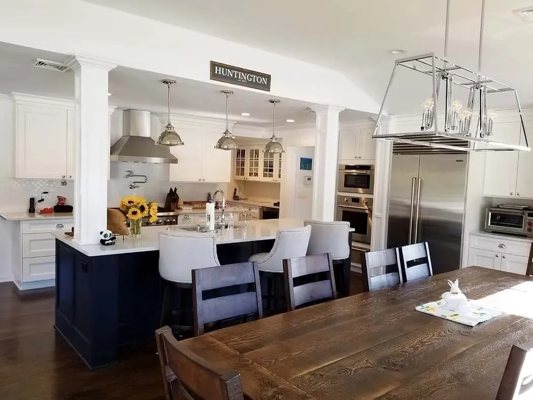 Renovated kitchen with a dark island, white cabinetry, and a wood dining table